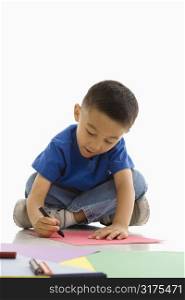 Asian boy sitting on floor coloring on paper.