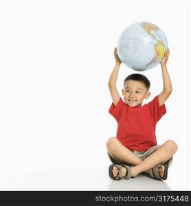 Asian boy sitting on floor holding Earth globe over his head.