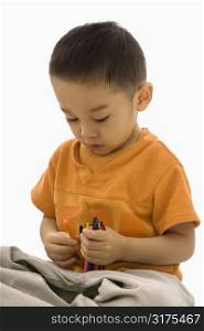 Asian boy sitting with handful of crayons.