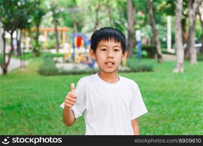 Asian boy thumbs up with playground in background.