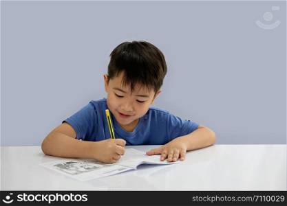 Asian boys are doing some writing on the book isolated on blue background.