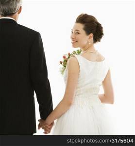 Asian bride looking over her shoulder while holding Caucasian groom&acute;s hand.