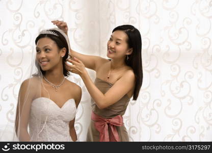 Asian bridesmaid adjusting veil of African-American bride.