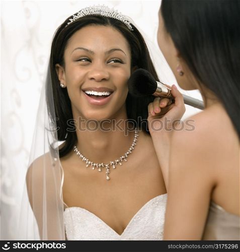 Asian bridesmaid applying makeup to African-American bride.