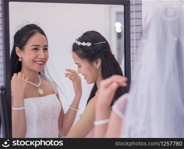 Asian bridesmaid helping adjust bride gown in dressing room on wedding day.