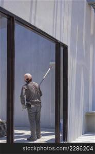 Asian builder worker using long handle roller brush to applying primer white paint on cement wall in door frame on concrete wall inside of house construction site