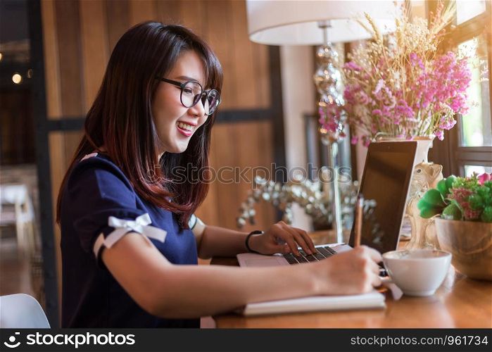 Asian business female working with laptop make a note in coffee shop like the background.