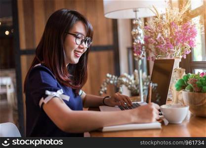 Asian business female working with laptop make a note in coffee shop like the background.