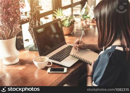 Asian business female working with make a note with a notebook and laptop in coffee shop like the background.
