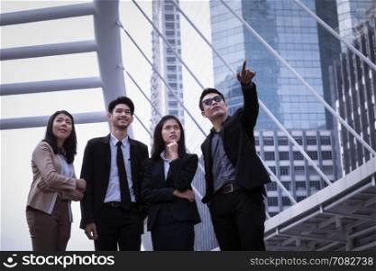 Asian business man and woman group standing on ground and to point the finger away and business city modern office building background