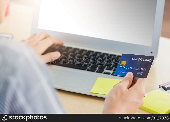 Asian business man hand holding credit card and typing entering security code on a laptop computer for process payment online shopping on the internet at the home office