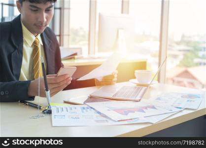 Asian business man hands typing on laptop computer keyboard with business graph diagram data paperwork ,mobile phone and cup of coffee on the desk at modern home office. Digital marketing concept.