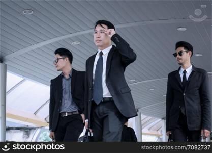 Asian business man with group of bodyguard walking on business street and looking away for safety and protection concept