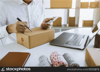 Asian business teenager is looking on tablet and writing a customer address contact to deliver the package to the customer at the destination.