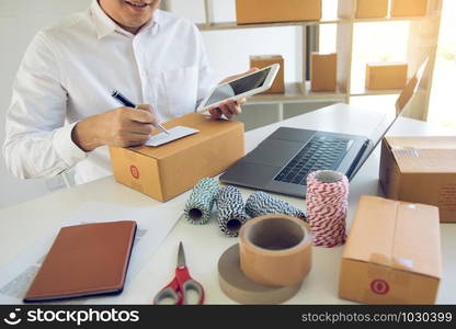 Asian business teenager is looking on tablet and writing a customer address contact to deliver the package to the customer at the destination.