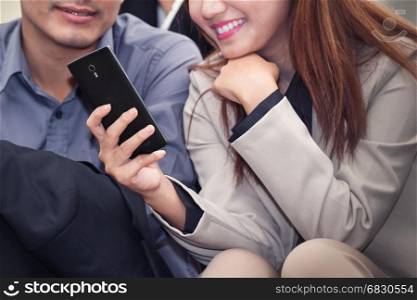 Asian business woman and man smiling and using cell phone together