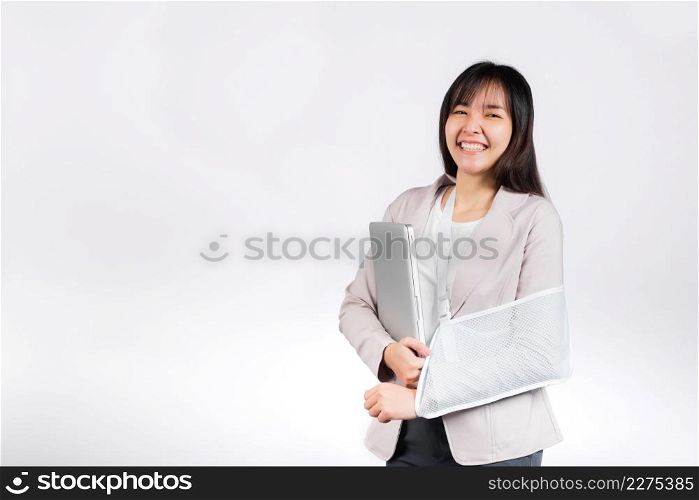 Asian business woman confident smiling broken arm after accident and wear arm splint for treatment but still have to work she hold laptop computer studio isolated on white background,copy space