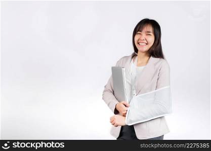 Asian business woman confident smiling broken arm after accident and wear arm splint for treatment but still have to work she hold laptop computer studio isolated on white background,copy space