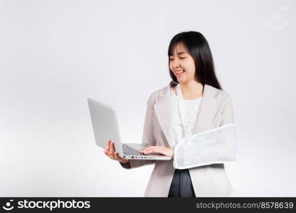 Asian business woman confident smiling broken arm after accident and wear arm splint for treatment but still have to work she hold laptop computer studio isolated on white background,copy space