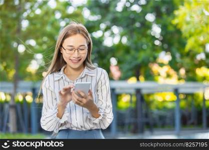Asian business woman happy smiling looking at smartphone standing park outdoor green nature background