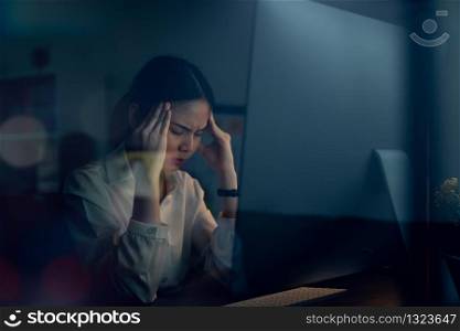 Asian business woman have a headache because using the computer and working for a long time at night.