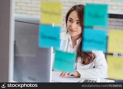 Asian Business woman holding coffee cup and working with technology computer and memo note on the mirror in happiness action at office or coworking space,startup and entrepreneur,workshop and strategy