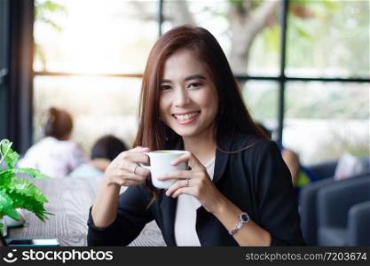 Asian business woman smiling and holding cup coffee for drinking at coffee cafe.
