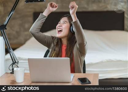 Asian business woman using technology laptop and working from home in indoor bedroom, listening the music and Dancing when work at home, social distance and self responsibility with quarantine concept