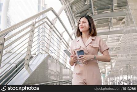 Asian business woman wearing formal suit for work while holding a cup of coffee, tablet and walking in the morning