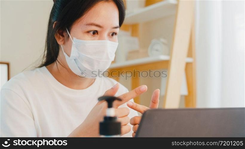 Asian business woman wearing mask using laptop working call video conference with customer in living room from home when social distancing stay at home and self quarantine time, coronavirus concept.