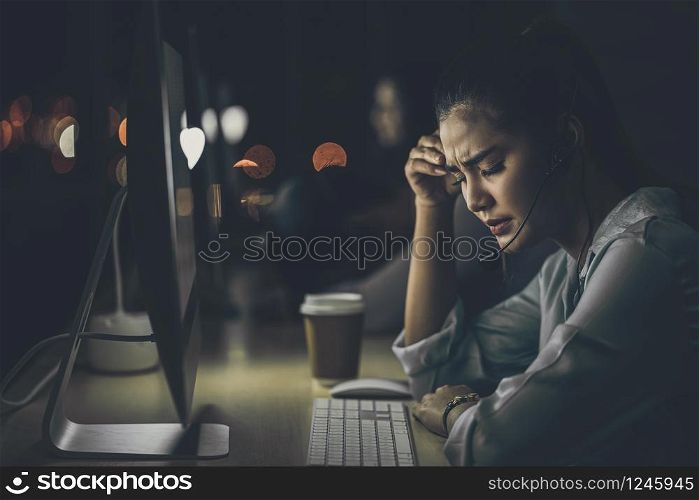 Asian business woman working hard late with her technology computer in office, customer service and call center department, hard worker and overtime,Stress and headache, low light environment,