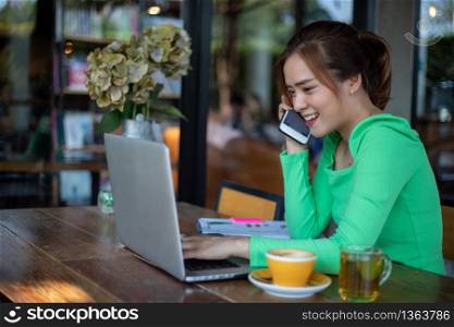 Asian Business women are using mobile and touch smart phone for Communication and women using notebook for working in coffee shop