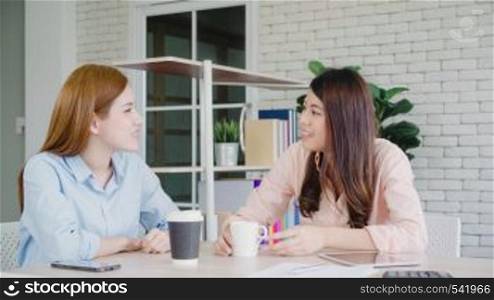 Asian business women enjoying drinking warm coffee, discuss about work and chit chat gossip while relax working in office. Smart business women social meeting concept.