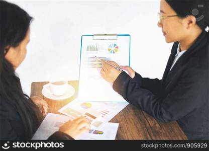 Asian business women working present the report graph financial information at the meeting in office the table desk / checking preparing sale report money analyzing graphs