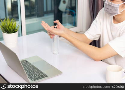 Asian business young handsome man glasses working from home office he quarantines disease coronavirus or COVID-19 wearing protective mask and cleaning hands with sanitizer gel on front laptop computer