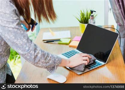 Asian Business young woman work from home office he cleaning laptop computer by sanitizer alcohol spray quarantines disease coronavirus or COVID-19 and wearing a protective mask before do job
