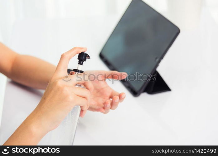 Asian Business young woman working from home office he quarantines disease coronavirus or COVID-19 wearing a protective mask and cleaning hands with sanitizer gel on front tablet computer