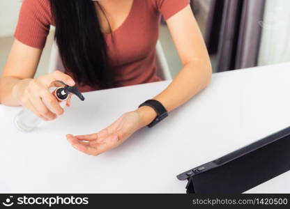 Asian Business young woman working from home office he quarantines disease coronavirus or COVID-19 wearing a protective mask and cleaning hands with sanitizer gel on front tablet computer