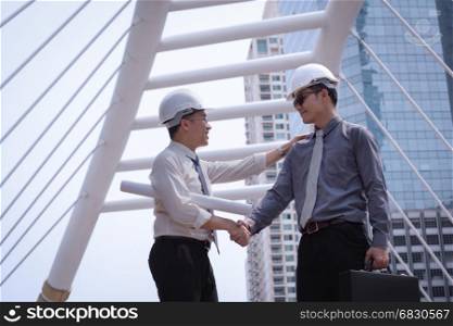 Asian businessman discuss and shake hand with engineer architect professional wearing safety helmet and suite, holding construction roll plan and briefcase for working team concept