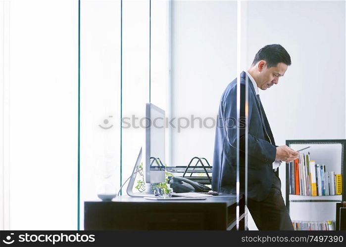 Asian businessman in the office standing and using a digital tablet to work .