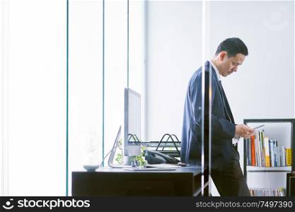 Asian businessman in the office standing and using a digital tablet to work .