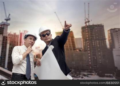 Asian businessman looking and point to finger away and engineer architect hold construction industrial plan background for working together as team concept
