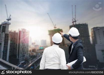 Asian businessman looking and point to finger away and engineer architect hold construction industrial plan background for working together as team concept, back view