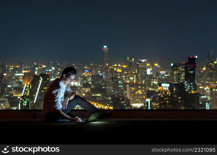 Asian businessman sitting and using the laptop over the cityscape background at night time, Business success and technology concept