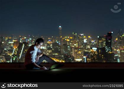 Asian businessman sitting and using the laptop over the cityscape background at night time, Business success and technology concept