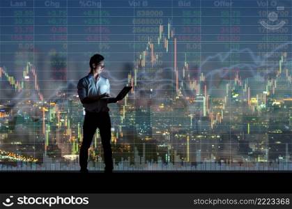 Asian businessman standing and using the smart mobile phone showing the Stock market chart over the cityscape background at night time, Business  technology and trading concept