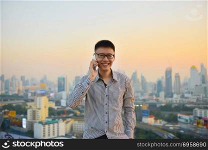 Asian businessman using phone with city background, technology communication concept. Asian businessman using phone with city background, technology