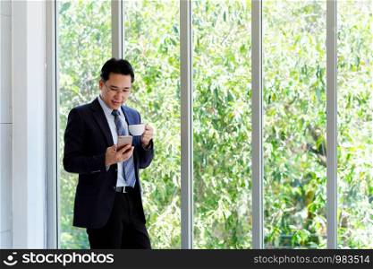 Asian businessman using smart phone and drinking coffee at office, office life and business concept
