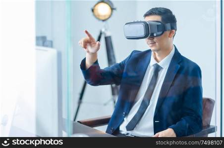 Asian businessman wearing virtual reality goggle and pointing up in a office .