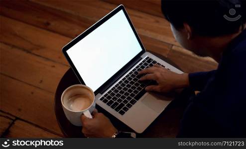 Asian businessman with casual clothing drinking coffee and working with white screen laptop in coffee cafe with low light environment, Lifestyle and leisure concept